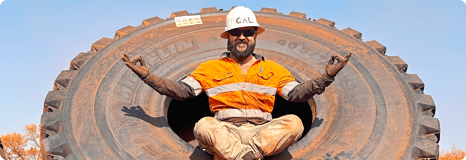 Cal sitting cross-legged in a giant haul truck tire on site